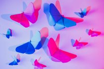 Mariposas rosadas y azules unidas a la pared lila sobre hoja de papel tallada - foto de stock