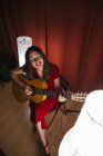 From above talented woman in red dress performing song and playing guitar in warm lighted stage nearby white lamp — Stock Photo