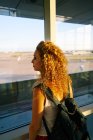 Vista trasera de mujer con estilo rizado con mochila observando el campo con aviones en el aeropuerto de Texas - foto de stock