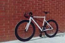 Nova bicicleta de estrada branca moderna com barra de alça preta estacionada contra a parede de tijolo vermelho — Fotografia de Stock