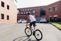 Uomo sportivo in piedi durante la guida di una bicicletta tra edifici collegati in estate giornata di sole — Foto stock