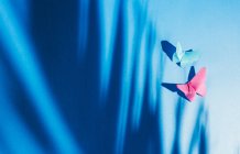 Papillons fragiles faits de papier avec une ombre de feuille de palmier attachée à une toile de soie bleue — Photo de stock