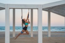 Весела жінка розтягує ногу на синьому гамаку для повітряної йоги на дерев'яній сцені — стокове фото