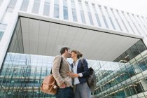 De baixo feliz casal colegas beijando uns aos outros, enquanto em pé fora edifício moderno na rua da cidade após o trabalho — Fotografia de Stock