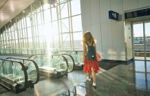 Вид сзади очаровательной кудрявой женщины в красной юбке с рюкзаком, спускающейся по эскалатору в аэропорту Техаса — стоковое фото