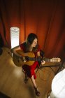 From above talented woman in red dress performing song and playing guitar in warm lighted stage nearby white lamp — Stock Photo