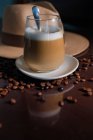 Стакан горячего напитка в композиции со шляпой и зерном кофе на деревянном столе — стоковое фото