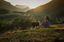 Turista adulto con cane contro la verde valle boscosa sotto il cielo limpido in estate — Foto stock