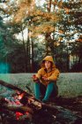 Mujer viajera calentando manos cerca de fogata en el claro del bosque - foto de stock
