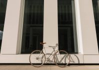 Bicicleta aparcada en la acera cerca de la pared del edificio contemporáneo en el día soleado en la calle de la ciudad - foto de stock