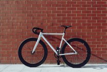 New modern white road bicycle with black handle bar parked against red brick wall — Stock Photo