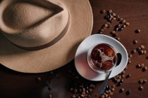 Стакан горячего напитка в композиции со шляпой и зерном кофе на деревянном столе — стоковое фото