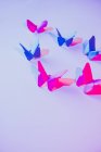 Розовые и голубые бабочки, прикрепленные к лиловой стене над резным листком бумаги — стоковое фото