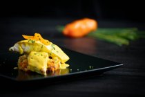 Gastronomia sana Corvina con salsa al pepe giallo in elegante piatto nero a tavola — Foto stock