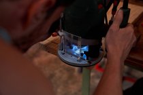 Immagine ritagliata dell'uomo utilizzando fresatrice per la lavorazione di tavole di legno mentre si lavora sul posto di lavoro — Foto stock