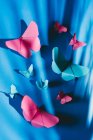 Гибкие бабочки из бумаги с тенью листьев пальмы, прикрепленной к синему шелку. — стоковое фото