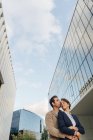Знизу щаслива пара колег поцілунки один одного, стоячи за межами сучасної будівлі на міській вулиці після роботи — стокове фото