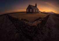 Semplice edificio della chiesa situato dietro la vecchia recinzione in pietra contro il luminoso cielo al tramonto in Islanda — Foto stock