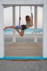 Веселая женщина, растягивающая ногу на голубом гамаке для воздушной йоги на деревянной сцене — стоковое фото