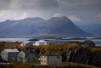 Bonitas casas situadas en la orilla del mar cerca de la cresta de la montaña en el día nublado en Islandia - foto de stock