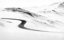 Camino curvilíneo de asfalto que atraviesa colinas blancas y nevadas en el día de invierno en Islandia - foto de stock