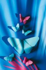 Fragile butterflies made of paper with palm tree leaf shadow attached to blue silk fabric — Stock Photo