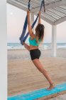 Femme gaie étirant la jambe sur hamac bleu pour le yoga aérien sur scène en bois — Photo de stock