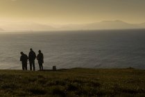 Group of travelers standing on coast of peaceful sea with mountains silhouette in morning time — Stock Photo