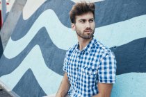 Cheerful young male in casual plaid shirt looking away with painted wall on background — Stock Photo