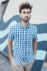 Jovem alegre macho em camisa xadrez casual olhando para longe com parede pintada no fundo — Fotografia de Stock