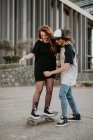 Lachende Teenager und Mädchen, die Skaten lernen und Spaß auf der Straße haben — Stockfoto