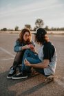 Casal adolescente na moda sentado em patins em estrada remota vazia e falando olhando um para o outro — Fotografia de Stock