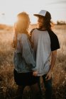 Jeunes adolescents élégants embrassant joyeusement wile debout dans un champ rural reculé avec la lumière du coucher du soleil chaud — Photo de stock