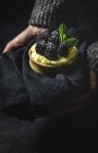 Person mit hausgemachtem kleinen Kuchen mit Brombeeren und köstlicher Creme aus Vanille und Minze auf dunklem Handtuch — Stockfoto