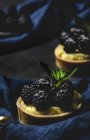 Close-up of homemade small cakes with blackberries and delicious cream of vanilla and mint on dark background — Stock Photo