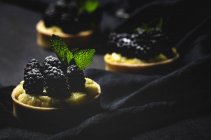 Nahaufnahme von hausgemachten kleinen Kuchen mit Brombeeren und köstlicher Creme aus Vanille und Minze auf dunklem Hintergrund — Stockfoto