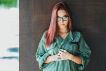 Zufriedener stilvoller Teenager mit Brille in dunkelgrünem Hemd neben brauner Wand und Blick in die Kamera — Stockfoto
