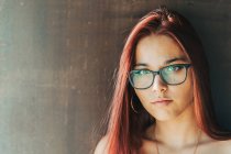 Content stylish teenager in glasses nearby brown wall looking at camera — Stock Photo