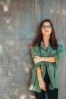 Contenu adolescent élégant dans des lunettes en chemise vert foncé à proximité mur brun regardant caméra — Photo de stock