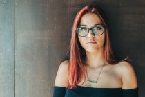 Content stylish teenager in glasses nearby brown wall looking at camera — Stock Photo