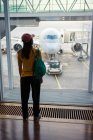 Vista trasera de una mujer irreconocible con gorra, mochila y ropa deportiva esperando en el aeropuerto - foto de stock