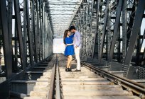 Liebender Mann und zarte Frau in blauem Kleid umarmen sich auf Eisenbahn unter Metallbrücke — Stockfoto