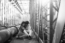 Homem amoroso e mulher macia em vestido azul abraçando na ferrovia sob construção de ponte de metal — Fotografia de Stock
