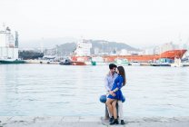 Vista lateral da mulher encantadora em vestido azul em abraço com homem bonito de ligação no cais do porto da cidade com navio no fundo — Fotografia de Stock