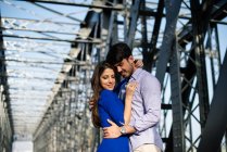 Uomo amorevole e tenera donna in abito blu che abbraccia sulla ferrovia sotto la costruzione di ponti in metallo — Foto stock