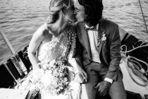 Задоволені одружені коханці в одязі цілуються, відпочиваючи на човні з морем на фоні — стокове фото