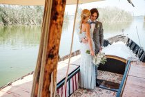 Zufriedene verheiratete Liebhaber in Hochzeitskleidung entspannen sich auf einem Boot mit Meer im Hintergrund — Stockfoto