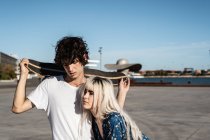 Attractive sensual blond woman with closed eyes embracing dark haired young man in white shirt holding skateboard — Stock Photo