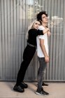 Вид збоку модна пара підтримує один одного, в той час як жінка спирається на хлопця назад проти смугастої стіни сучасної будівлі — стокове фото