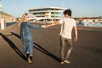 Back view of pensive blond walking woman looking back over shoulder and holding hand of handsome man — Stock Photo